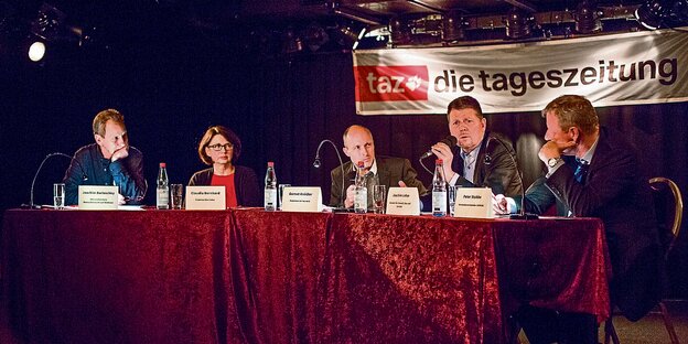 Die Teilnehmer des taz Salons sitzen an einem Tisch auf einer Bühne im Lagerhaus. Die Teilnehmer des taz Salons sitzen an einem Tisch auf einer Bühne im Lagerhaus.