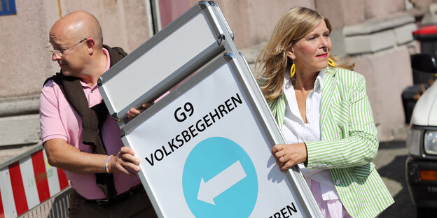 Ein Mann und eine Frau stellen ein Schild der Initiative "G9-Jetzt-HH" auf. Ein Mann und eine Frau stellen ein Schild der Initiative "G9-Jetzt-HH" auf.