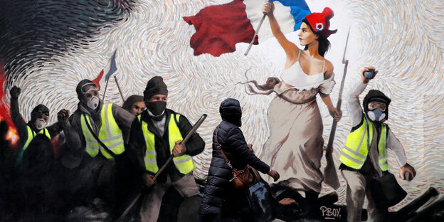 Eine Frau geht vor einem Wandgemälde auf einer Mauer vorbei, auf dem Gelbwesten-Demonstranten zu sehen sind Eine Frau geht vor einem Wandgemälde auf einer Mauer vorbei, auf dem Gelbwesten-Demonstranten zu sehen sind