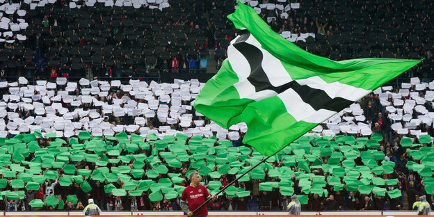 Mann schwenkt Fahne in Vereinsfarben schwarz-weiß-grün vor Fanblock von Hannover 96 Mann schwenkt Fahne in Vereinsfarben schwarz-weiß-grün vor Fanblock von Hannover 96