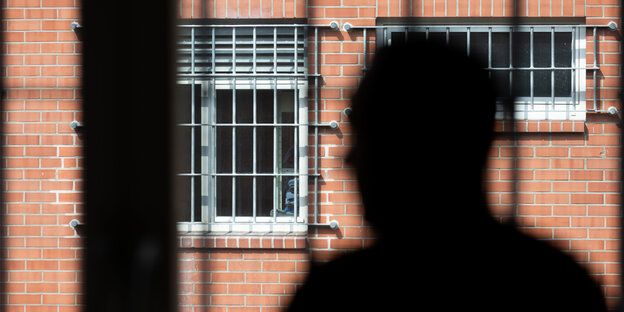 Vor vergitterten Fentsern ist der Schatten eines Kopfes zu sehen Vor vergitterten Fentsern ist der Schatten eines Kopfes zu sehen