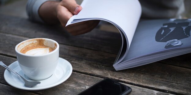 Eine Person liest, daneben steht eine Tasse Kaffee Eine Person liest, daneben steht eine Tasse Kaffee