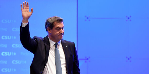 Markus Söder winkt vor blauem Hintergrund Markus Söder winkt vor blauem Hintergrund