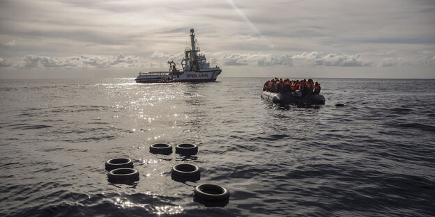 Ein Boot mit Menschen darauf, im Hintergrund ein Schiff Ein Boot mit Menschen darauf, im Hintergrund ein Schiff