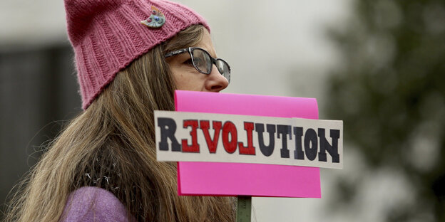 Eine Frau mit pinker Mütze und einem Schild, auf dem "Revolution" steht. Eine Frau mit pinker Mütze und einem Schild, auf dem "Revolution" steht.