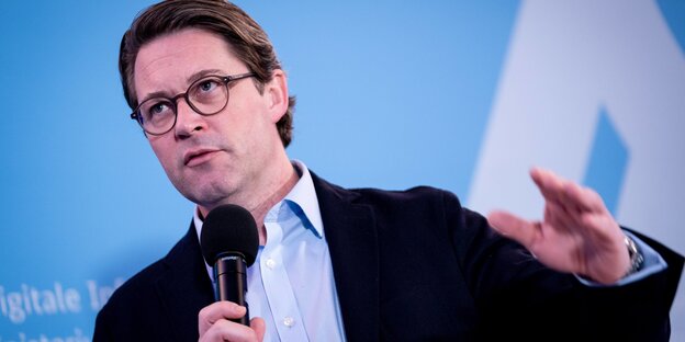 Ein Mann im Anzug spricht in ein Mikrofon und gestikuliert Ein Mann im Anzug spricht in ein Mikrofon und gestikuliert