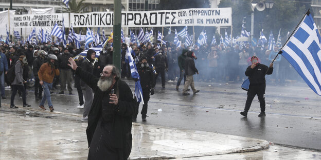 Auf den Straßen Athens protestieren Menschen mit Griechenland-Flaggen. Sie tragen Gasmasken Auf den Straßen Athens protestieren Menschen mit Griechenland-Flaggen. Sie tragen Gasmasken