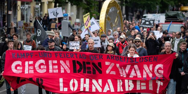 Menschen laufen vor einem Transparent mit der Aufschrift „Gegen den Zwang zur Lohnarbeit“