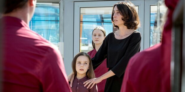 Eine Frau steht hinter einem Mädchen und hält ihre Hände auf der Schulter des Mädchens Eine Frau steht hinter einem Mädchen und hält ihre Hände auf der Schulter des Mädchens