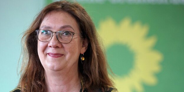 Eine Frau mit langen Haaren und Brille vor dem Logo der Grünen Eine Frau mit langen Haaren und Brille vor dem Logo der Grünen