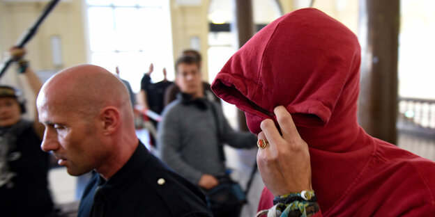 Ein Polizeibeamter führt einen Mann, der seinen Kopf in einem Kapuzenpulli verbirgt. Ein Polizeibeamter führt einen Mann, der seinen Kopf in einem Kapuzenpulli verbirgt.