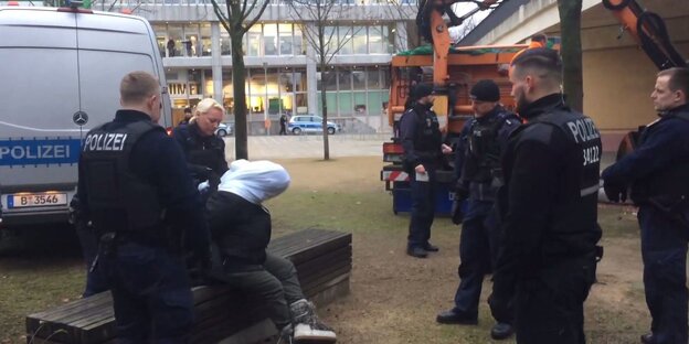 Polizisten ziehen einer obdachlosen Frau ein Tuch über den Kopf, während ihr Hab und Gut in den Müll wanderte Polizisten ziehen einer obdachlosen Frau ein Tuch über den Kopf, während ihr Hab und Gut in den Müll wanderte