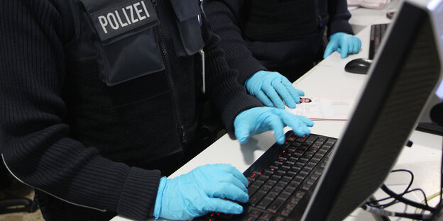 Polizisten mit Handschuhen tippen auf einer Tastatur Polizisten mit Handschuhen tippen auf einer Tastatur