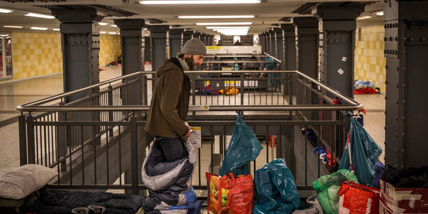 Ein Mann steht in einem U-Bahnhof zwischen Schlafsäcken und Tüten. Im Hintergrund sind Isomatten und weitere Schlafsäcke zu sehen Ein Mann steht in einem U-Bahnhof zwischen Schlafsäcken und Tüten. Im Hintergrund sind Isomatten und weitere Schlafsäcke zu sehen