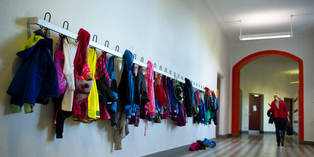 Eine Lehrerin geht über einen Schulflur, an der Garderobe hängen Kinderjacken. Eine Lehrerin geht über einen Schulflur, an der Garderobe hängen Kinderjacken.
