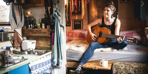 Eine Person sitzt mit einer Gitarre auf einem Bett Eine Person sitzt mit einer Gitarre auf einem Bett