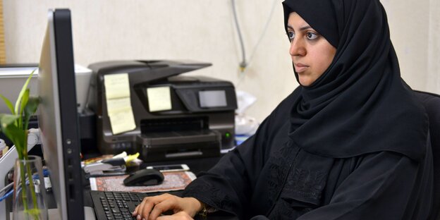 Eine Frau in einer saudischen Abaja sitzt an einem Computer. Eine Frau in einer saudischen Abaja sitzt an einem Computer.