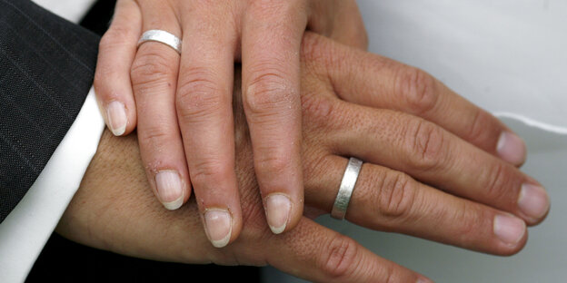Zwei Hände von zwei Personen liegen übereinander, an jeder Hand ein Ehering Zwei Hände von zwei Personen liegen übereinander, an jeder Hand ein Ehering
