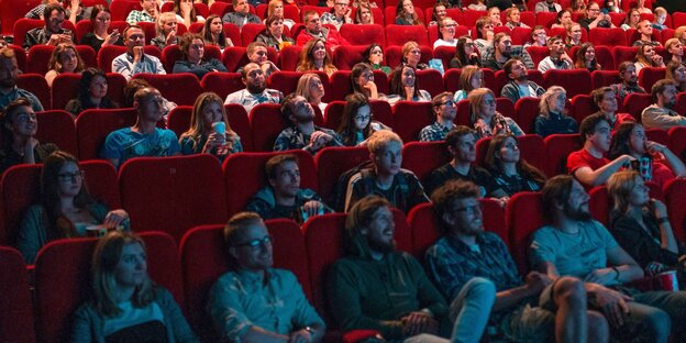 Menschen sitzen im Kinosaal und schauen auf die Leinwand Menschen sitzen im Kinosaal und schauen auf die Leinwand