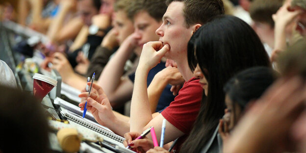 Studierende sitzen im Hörsaal und schreiben mit Studierende sitzen im Hörsaal und schreiben mit