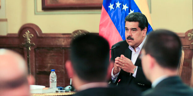Nicolas Maduro sitzt an ein em Schreibtisch, mehrere Menshcen hören ihm zu Nicolas Maduro sitzt an ein em Schreibtisch, mehrere Menshcen hören ihm zu