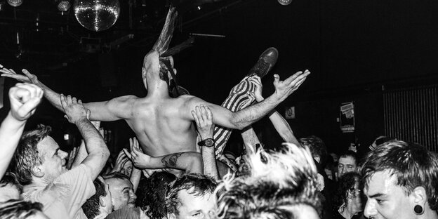 Die Schwarzweißaufnahme zeigt einen Mann mit Iro, der sich von der Menge durch den Berliner Punkclub SO36 tragen lässt. Nicht im Bild die Band: Die UK Subs gibt es schon seit über vierzig Jahren. Die Schwarzweißaufnahme zeigt einen Mann mit Iro, der sich von der Menge durch den Berliner Punkclub SO36 tragen lässt. Nicht im Bild die Band: Die UK Subs gibt es schon seit über vierzig Jahren.