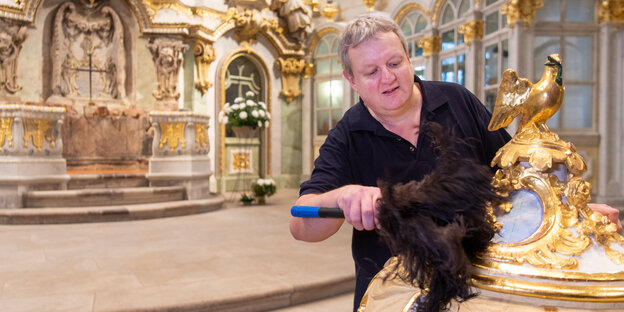 Ein Mann putzt in der Dresdner Frauenkirche den Golddeckel eines Taufbeckens. Was und ob er glaubt, ist nicht zu erkennen