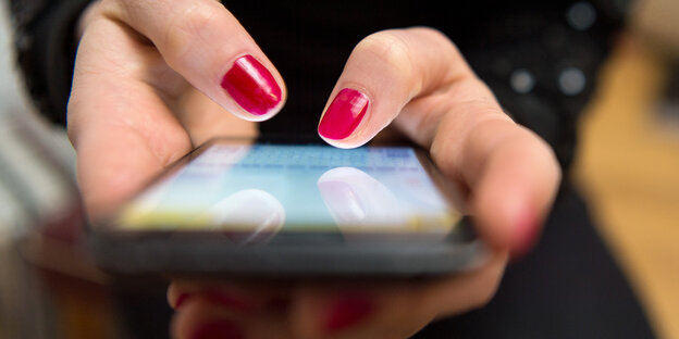 Eine Frau mit rot lackierten Fingernägeln hält ein Smartphone in der Hand Eine Frau mit rot lackierten Fingernägeln hält ein Smartphone in der Hand