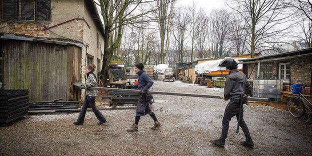 Drei Menschen tragen einen Stahlträger über das Gelände des Gewerbehofes Ratiborstraße in Kreuzberg