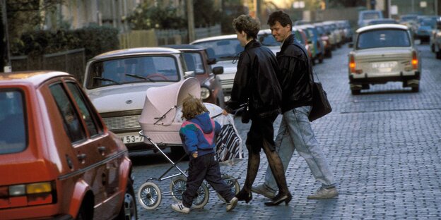 Ein junges Paar aus Mann und Frau überquert mit Kinderwagen eine Straße Ein junges Paar aus Mann und Frau überquert mit Kinderwagen eine Straße