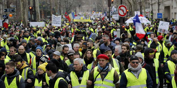 Eine Menschenmasse läuft durch Paris, alle tragen gelbe Westen und einige schwenken Frankreich-Fahnen Eine Menschenmasse läuft durch Paris, alle tragen gelbe Westen und einige schwenken Frankreich-Fahnen