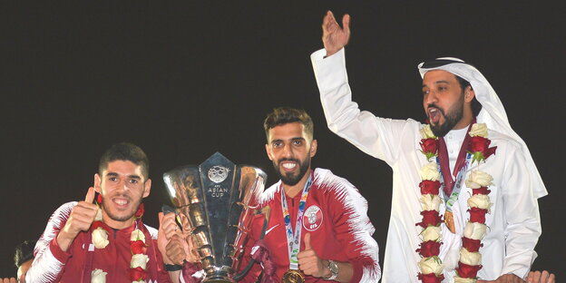 zwei Fußballer halten einen Pokal, daneben steht ein Mann mit erhobenem Arm zwei Fußballer halten einen Pokal, daneben steht ein Mann mit erhobenem Arm
