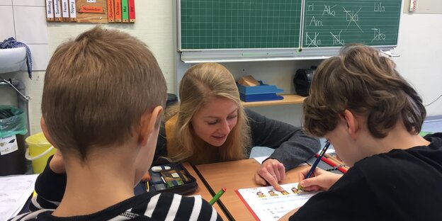 Eine junge Lehrerin hilft zwei Schülern in einem Klassenzimmer. Eine junge Lehrerin hilft zwei Schülern in einem Klassenzimmer.