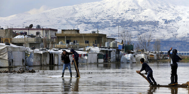 Flüchtlingszelte vor Gebäuden, im Hintergrund Berge, im Vordergrund Wasser Flüchtlingszelte vor Gebäuden, im Hintergrund Berge, im Vordergrund Wasser