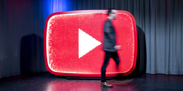Youtube-Logo als Bühnenskulptur, ein Mann geht schnell daran vorbei Youtube-Logo als Bühnenskulptur, ein Mann geht schnell daran vorbei