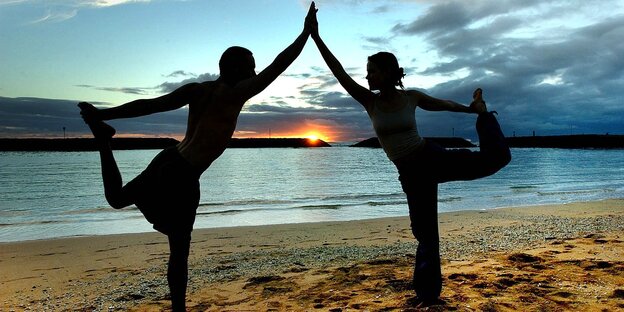 Zwei Menschen machen Yoga am Strand Zwei Menschen machen Yoga am Strand