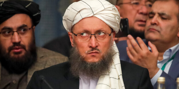 Bärtiger Mann mit Turban auf dem Kopf verdreht die Augen. Hinter im sind weitere Männer zu sehen. Bärtiger Mann mit Turban auf dem Kopf verdreht die Augen. Hinter im sind weitere Männer zu sehen.