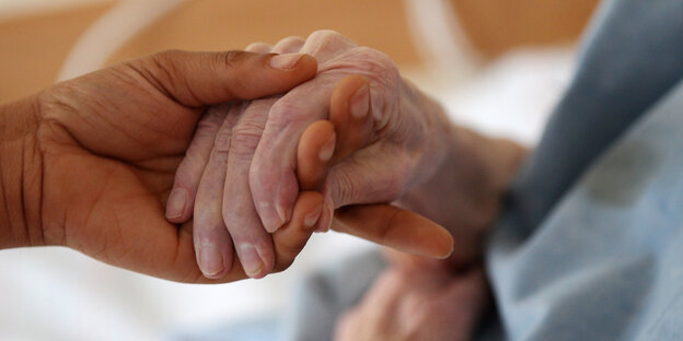 Pflegerin am Bett hält Hand von Bewohnerin Pflegerin am Bett hält Hand von Bewohnerin
