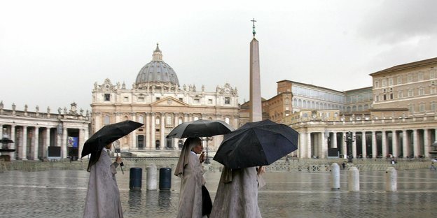 Drei Nonnen laufen bei Regen mit Regenschirmen über einen Platz Drei Nonnen laufen bei Regen mit Regenschirmen über einen Platz