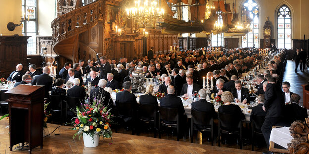 Männer sitzen in langen Reihen an einer festlich gedeckten Tafel.