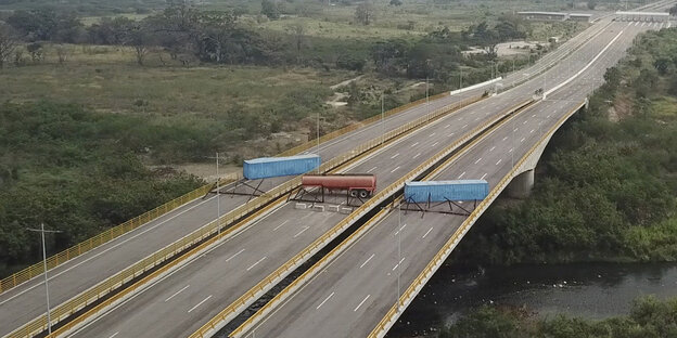 Die Fahrbahn einer mehrspurigen Autobahn ist auf der Brücke über einen Fluss durch einen Tanklaster und zwei Container versperrt. Die Fahrbahn einer mehrspurigen Autobahn ist auf der Brücke über einen Fluss durch einen Tanklaster und zwei Container versperrt.
