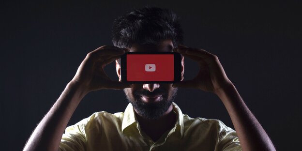 Mann hält sich Smartphone vor die Augen, Display zeigt zum Betrachter - auf ihm ist das Youtube-Logo zu sehen Mann hält sich Smartphone vor die Augen, Display zeigt zum Betrachter - auf ihm ist das Youtube-Logo zu sehen