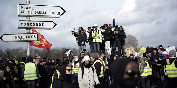 Viele Menschen, manche mit Gasmasken und maskiert - sie haben sich neben Pariser Straßenschildern versammelt Viele Menschen, manche mit Gasmasken und maskiert - sie haben sich neben Pariser Straßenschildern versammelt