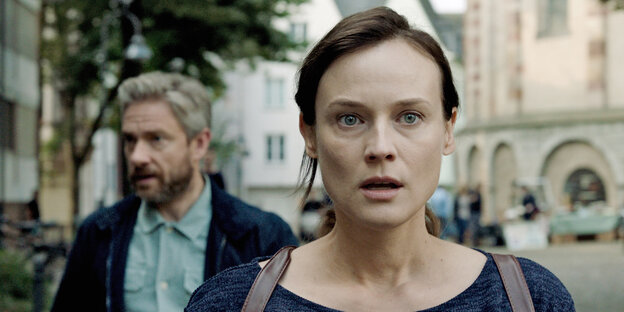Eine Frau mit starrem Blick, ein Mann im Hintergrund Eine Frau mit starrem Blick, ein Mann im Hintergrund