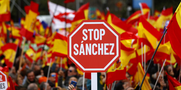 Vor zahlreichen spanischen Nationalflaggen wird ein Stoppschild mit der Aufschrift "Stop Sanchez" nach oben gehalten Vor zahlreichen spanischen Nationalflaggen wird ein Stoppschild mit der Aufschrift "Stop Sanchez" nach oben gehalten