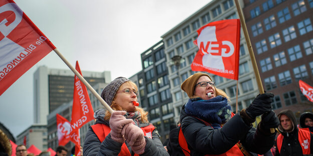Streikende schwenken Fahnen bei einer Kundgebung und pusten in Trillerpfeifen Streikende schwenken Fahnen bei einer Kundgebung und pusten in Trillerpfeifen