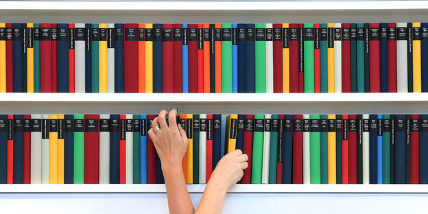 Zwei Menschen greifen überkreuz nach Büchern in einem Bücherregal Zwei Menschen greifen überkreuz nach Büchern in einem Bücherregal