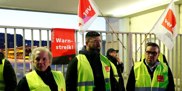 Drei Männer stehen in Warnwesten vor einem Zaun Drei Männer stehen in Warnwesten vor einem Zaun