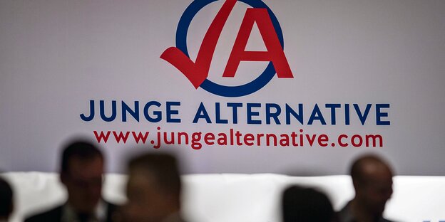 Menschen stehen vor einem wandfüllenden Logo der "Jungen Alternative". Menschen stehen vor einem wandfüllenden Logo der "Jungen Alternative".