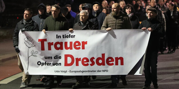 Männer die zusammen ein weißes Transparent mit Aufschrift vor sich hertragen - es ist abends